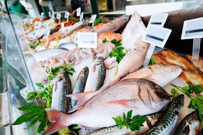 Assorted fresh seafood on ice at a market counter, with parsley garnishes and price tags.