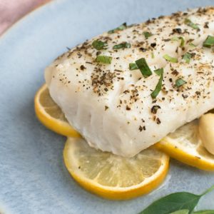 White fish fillet on lemon slices, garnished with herbs and pepper on a blue plate.