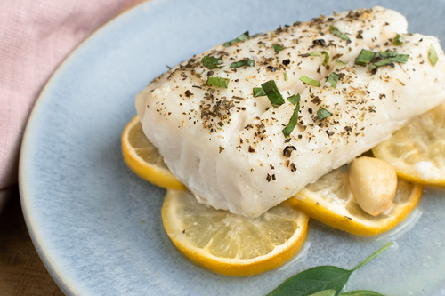 White fish fillet on lemon slices, garnished with herbs and pepper on a blue plate.